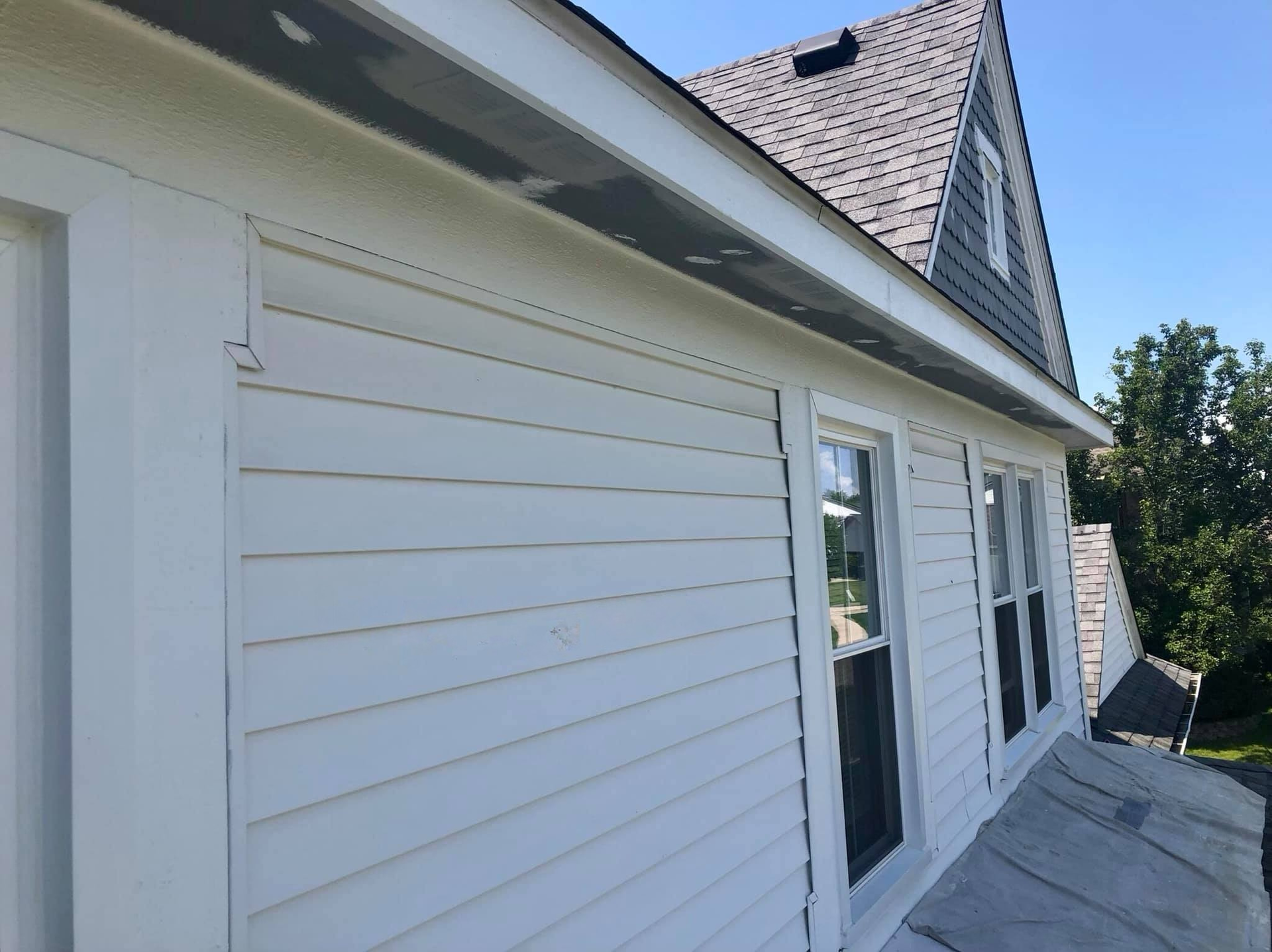 A low-angle view of the exterior wall, white siding, and roofline of a residential house under a clear blue sky.