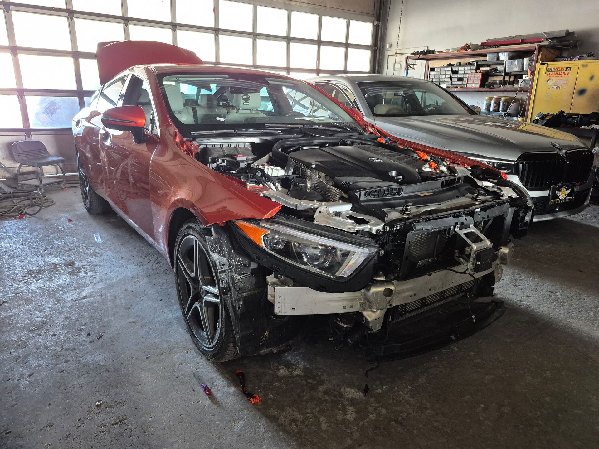 Red SUV with front-end damage in a garage, hood open and bumper removed