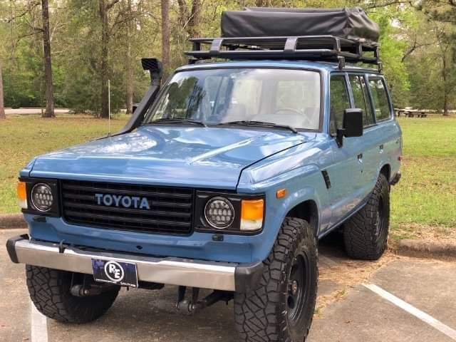Blue Toyota off-road SUV with roof cargo tent parked on a dirt road in a wooded area