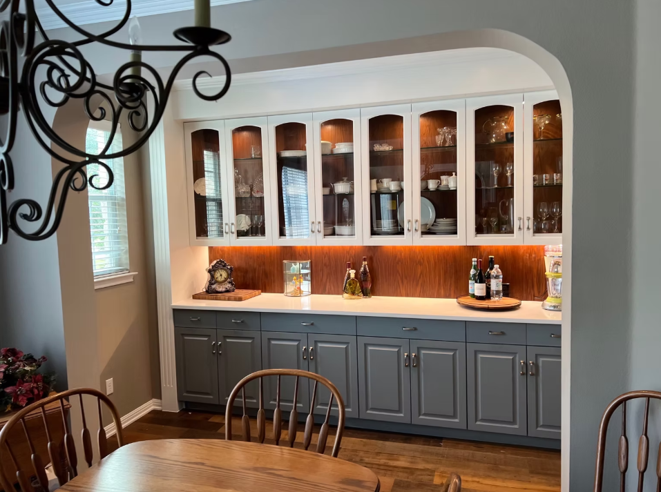 A dining room with a table , chairs , cabinets and a chandelier.