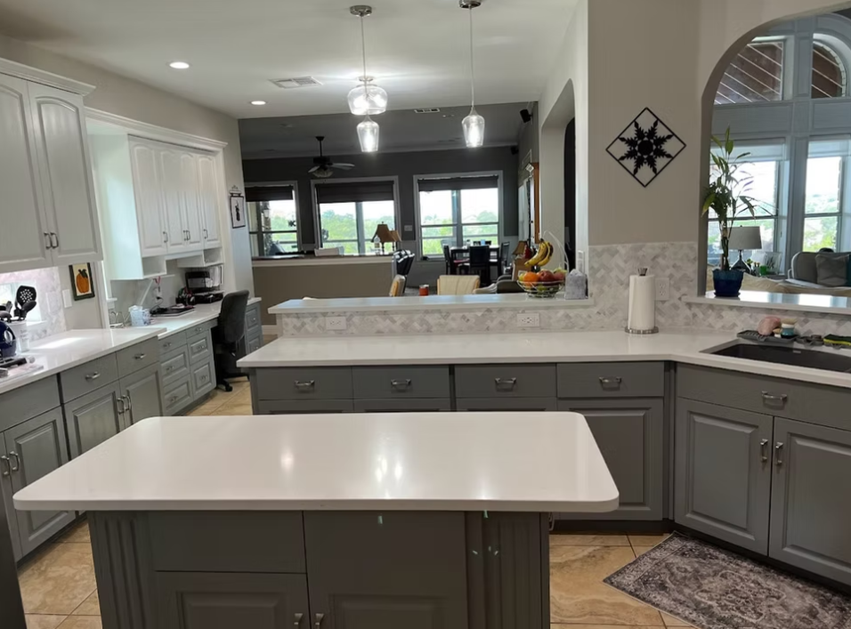 A kitchen with gray cabinets and white counter tops and a large island.