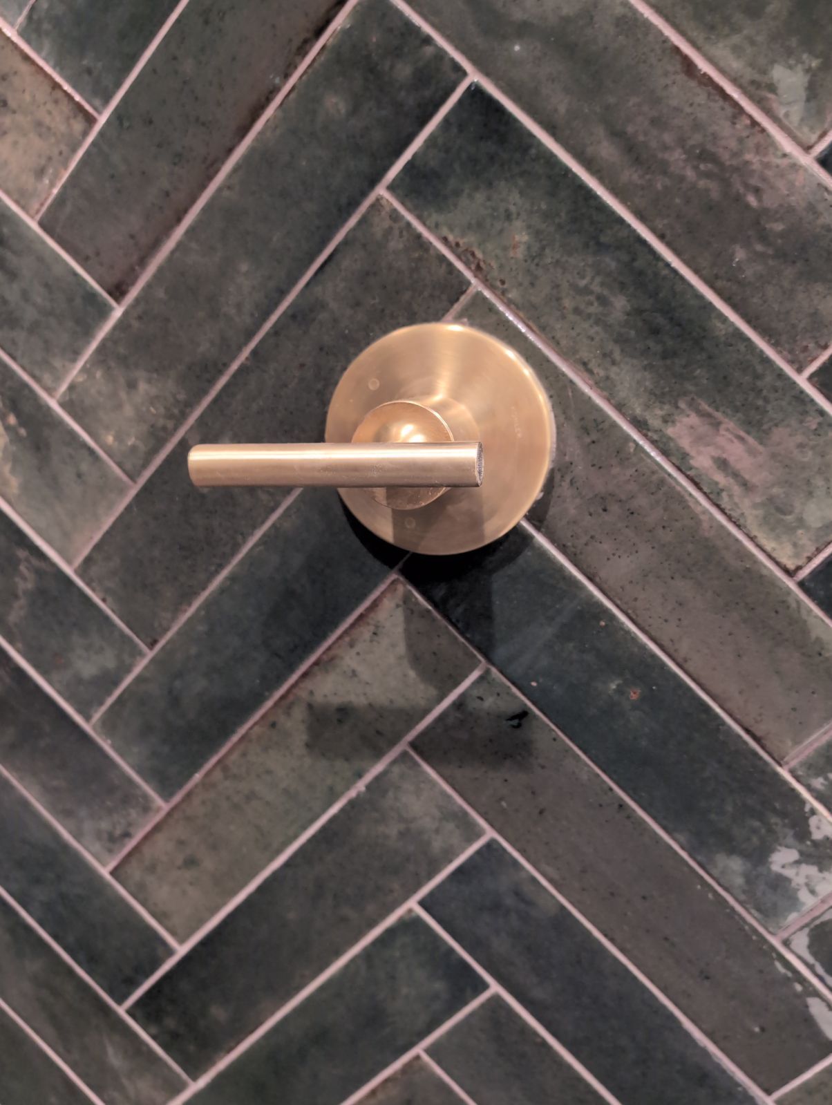 A close up of a door handle on a herringbone tile wall.