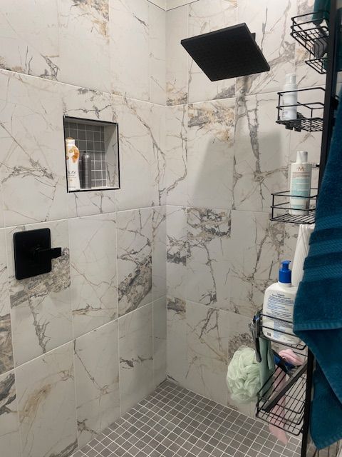 A shower with marble tiles and a black shower head.