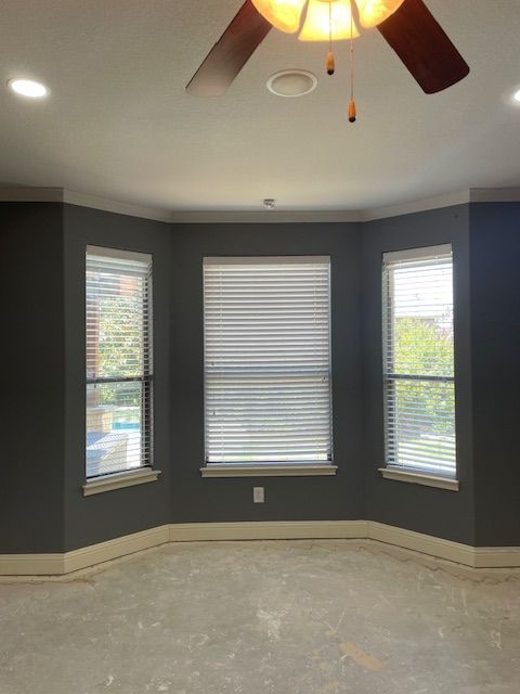 An empty room with a ceiling fan and three windows