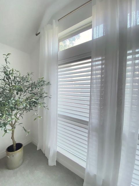 A potted plant is in front of a window with white curtains.