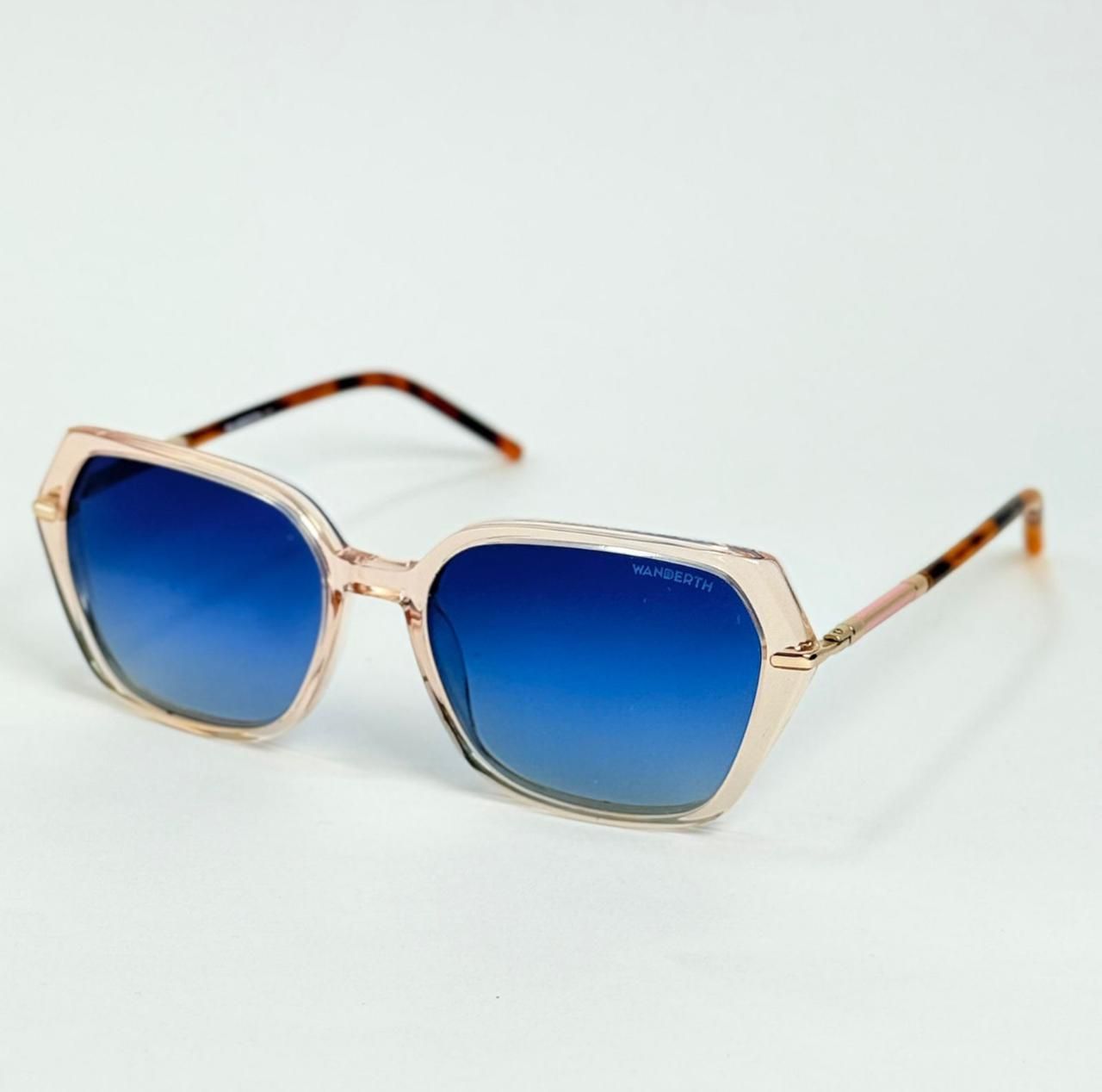 Gafas de sol con montura rosa y lentes azules sobre una superficie blanca. Patillas de carey y montura angular.