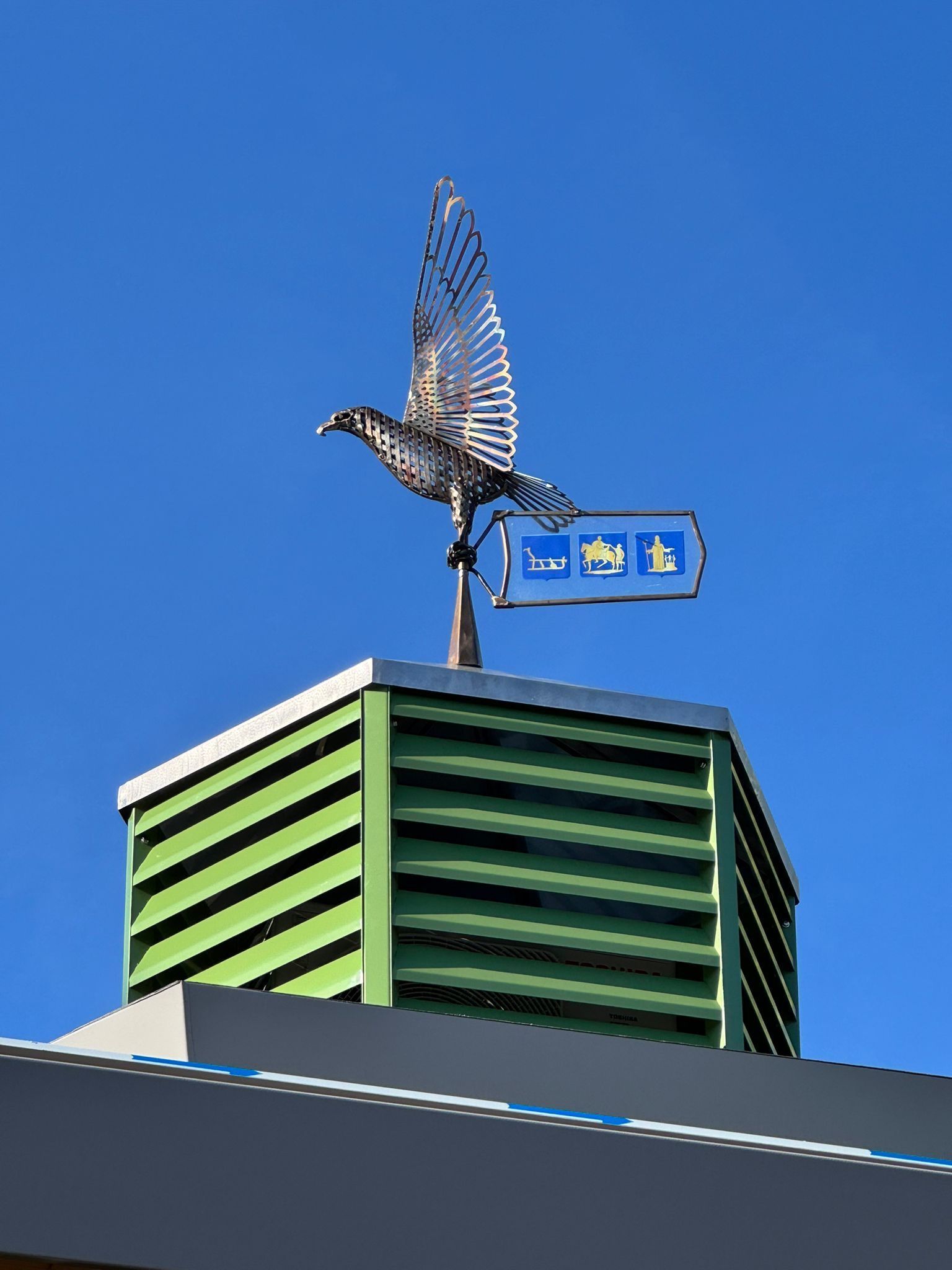 Een standbeeld van een vogel bovenop een groen gebouw