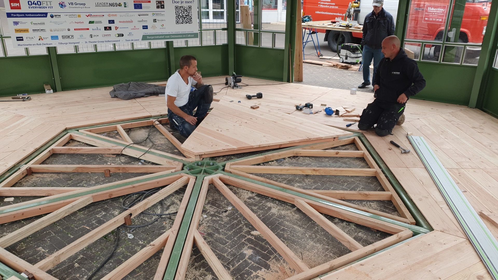 Twee mannen knielen op een houten vloer in een kamer.