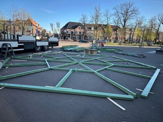 Op een parkeerplaats wordt een grote groene constructie gebouwd.