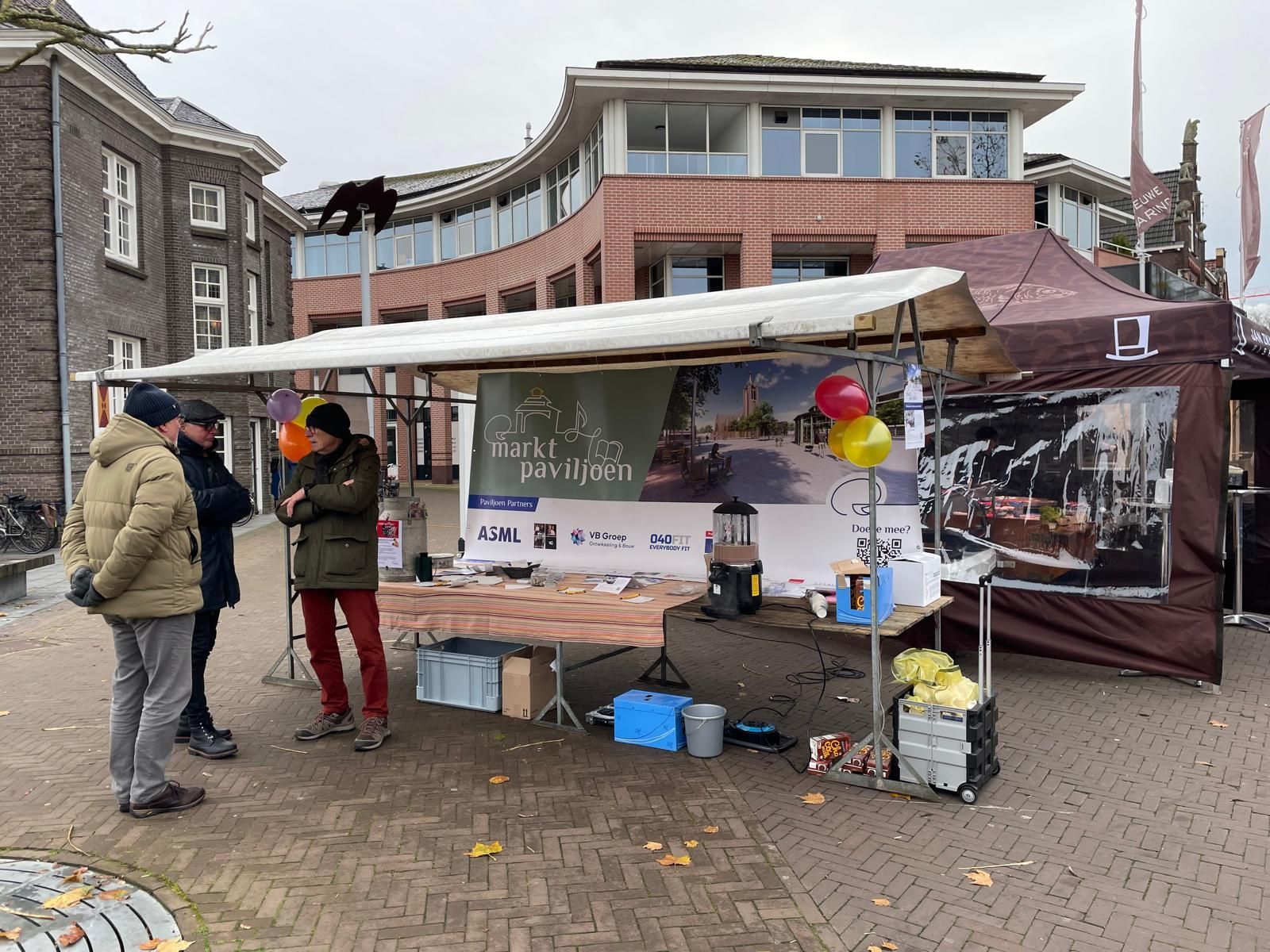 Een groep mensen die rond een tafel voor een gebouw staan.