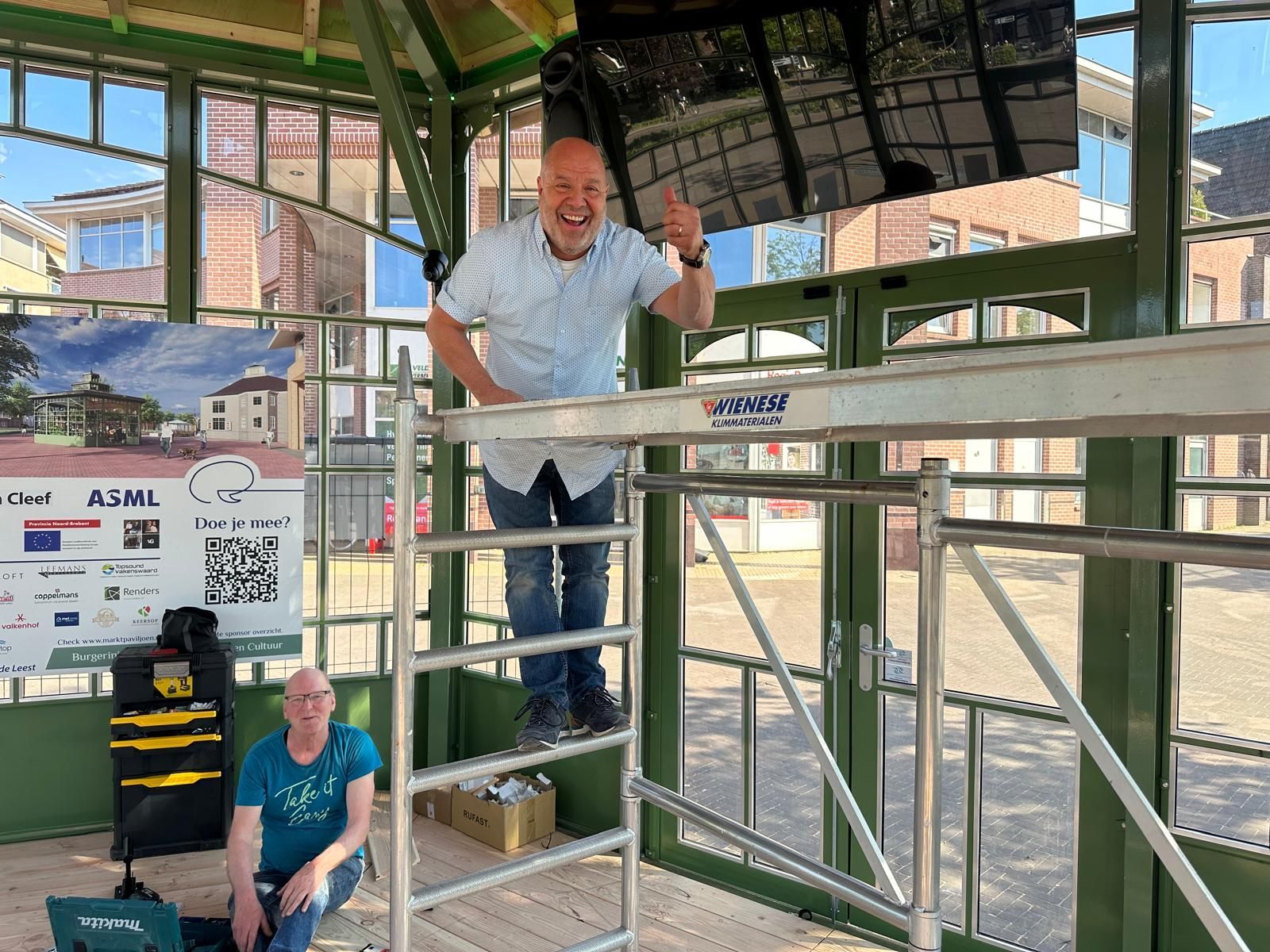 Twee mannen staan ​​op een steiger in een gebouw.