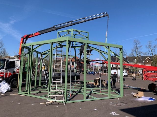 Een kraan tilt een groene structuur op een parkeerplaats op.