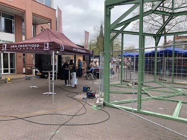 Een groep mensen staat onder een tent voor een gebouw.