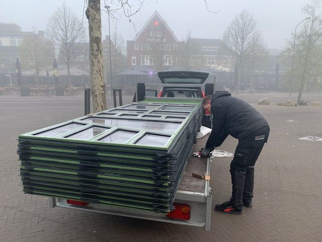 Een man laadt een oplegger met daarop een stapel groene deuren.