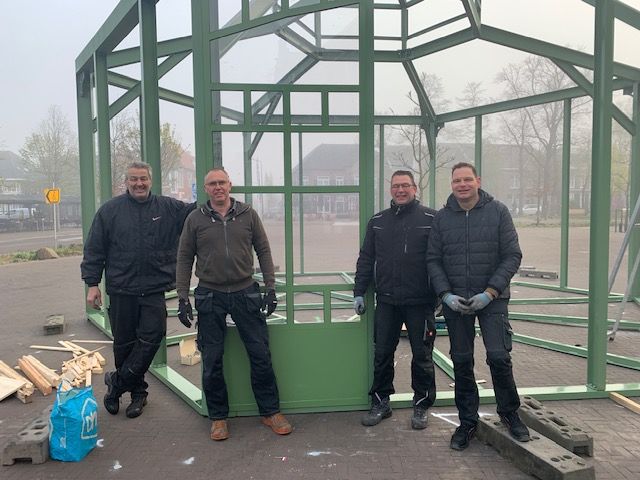 Een groep mannen staat voor een groene structuur.