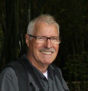 Een man met een bril en een snor lacht naar de camera