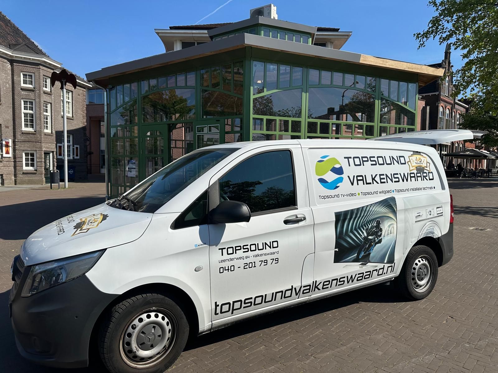 Een wit busje staat geparkeerd voor een gebouw.