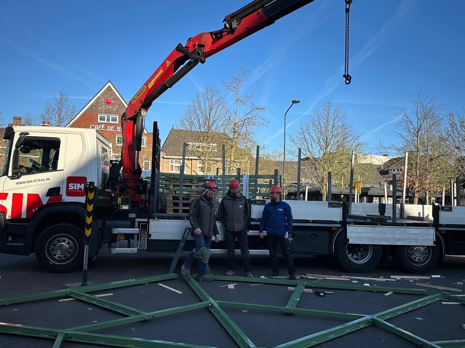 Drie mannen staan ​​voor een vrachtwagen met daaraan een kraan.