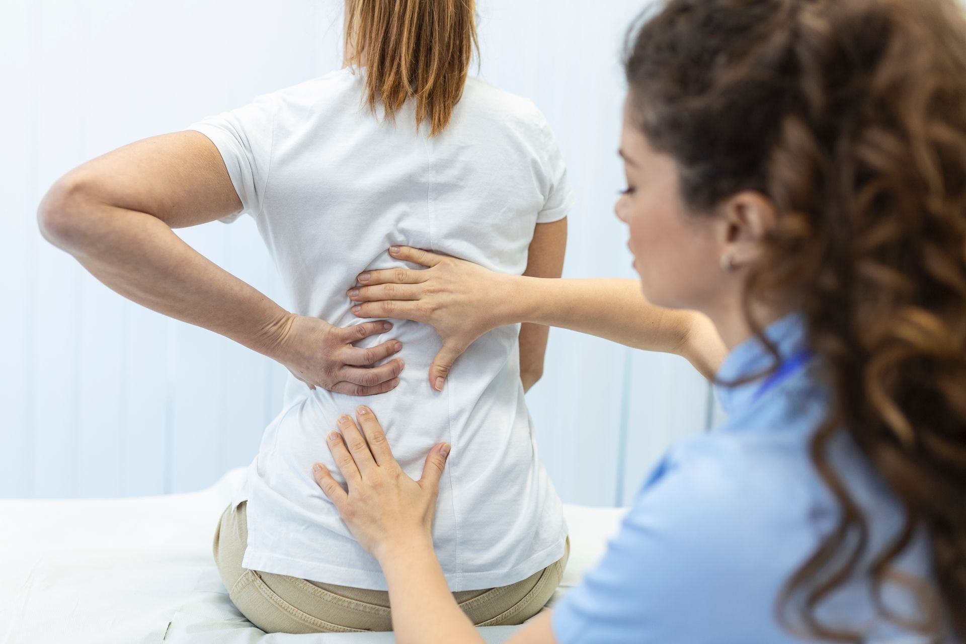 A woman is sitting on a bed while a doctor examines her back.