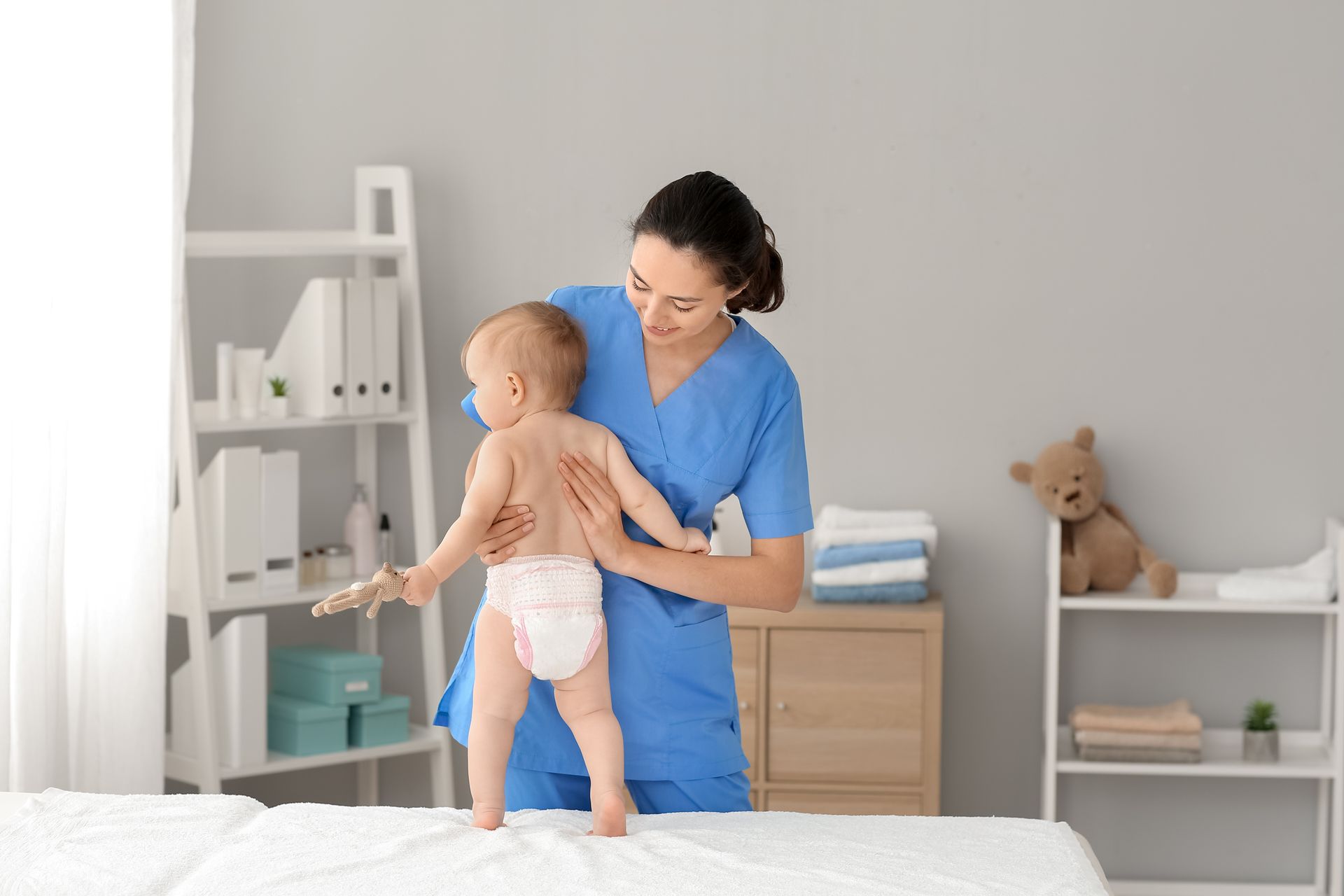 A nurse is holding a baby in a diaper on a bed.