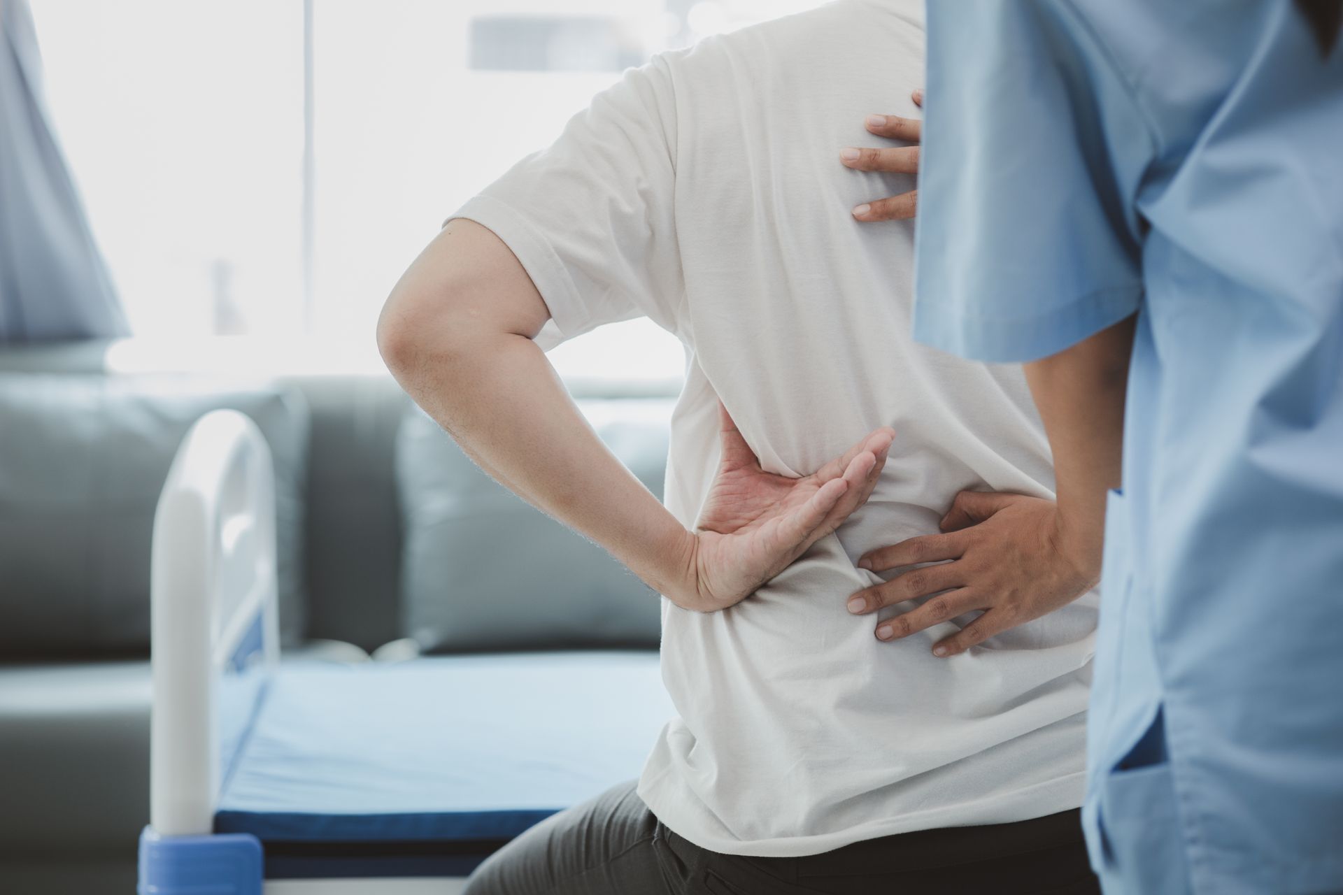 A nurse is helping a patient with back pain in a hospital room.