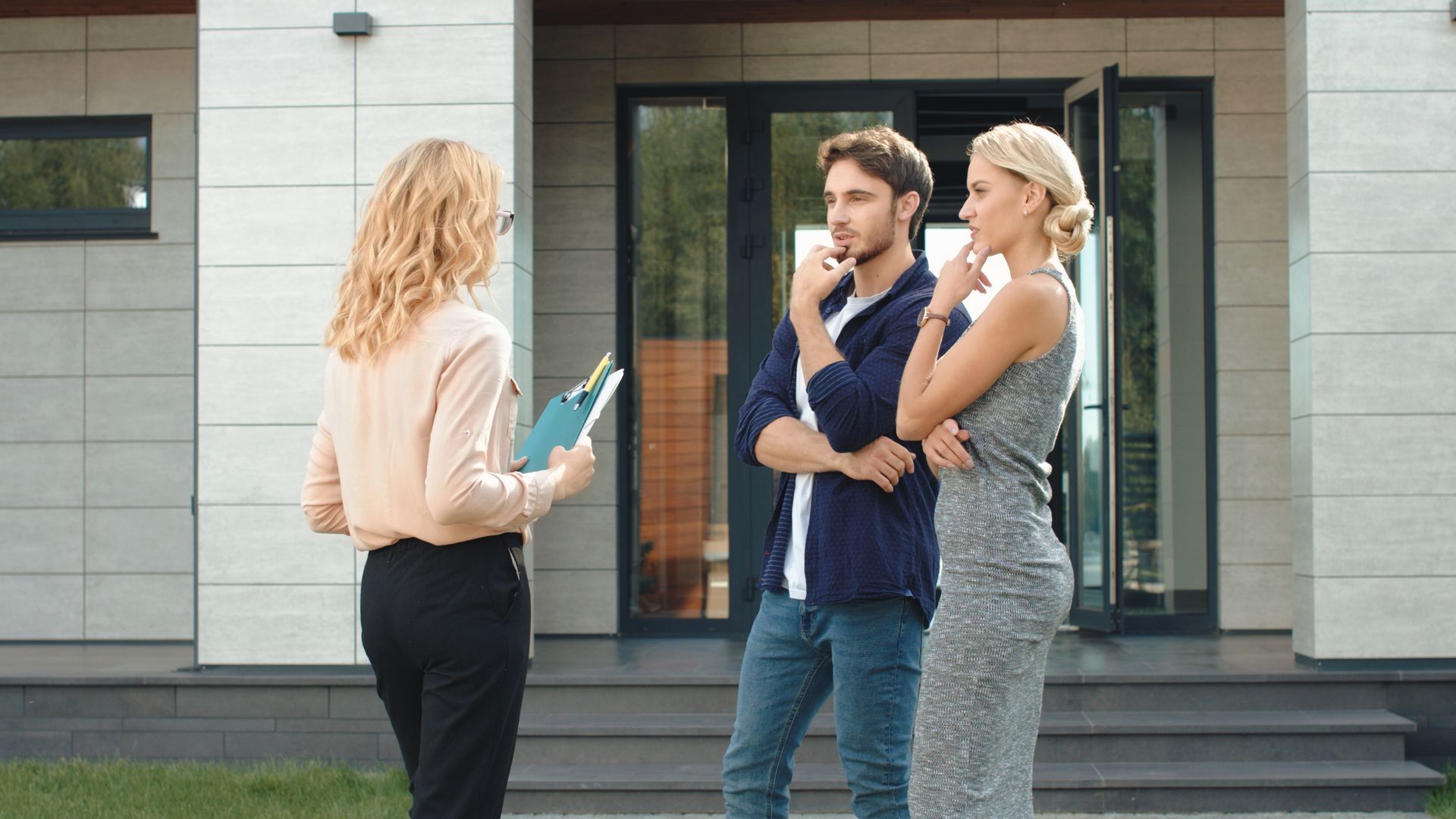 Three people talking outside a modern building, one holding a clipboard.