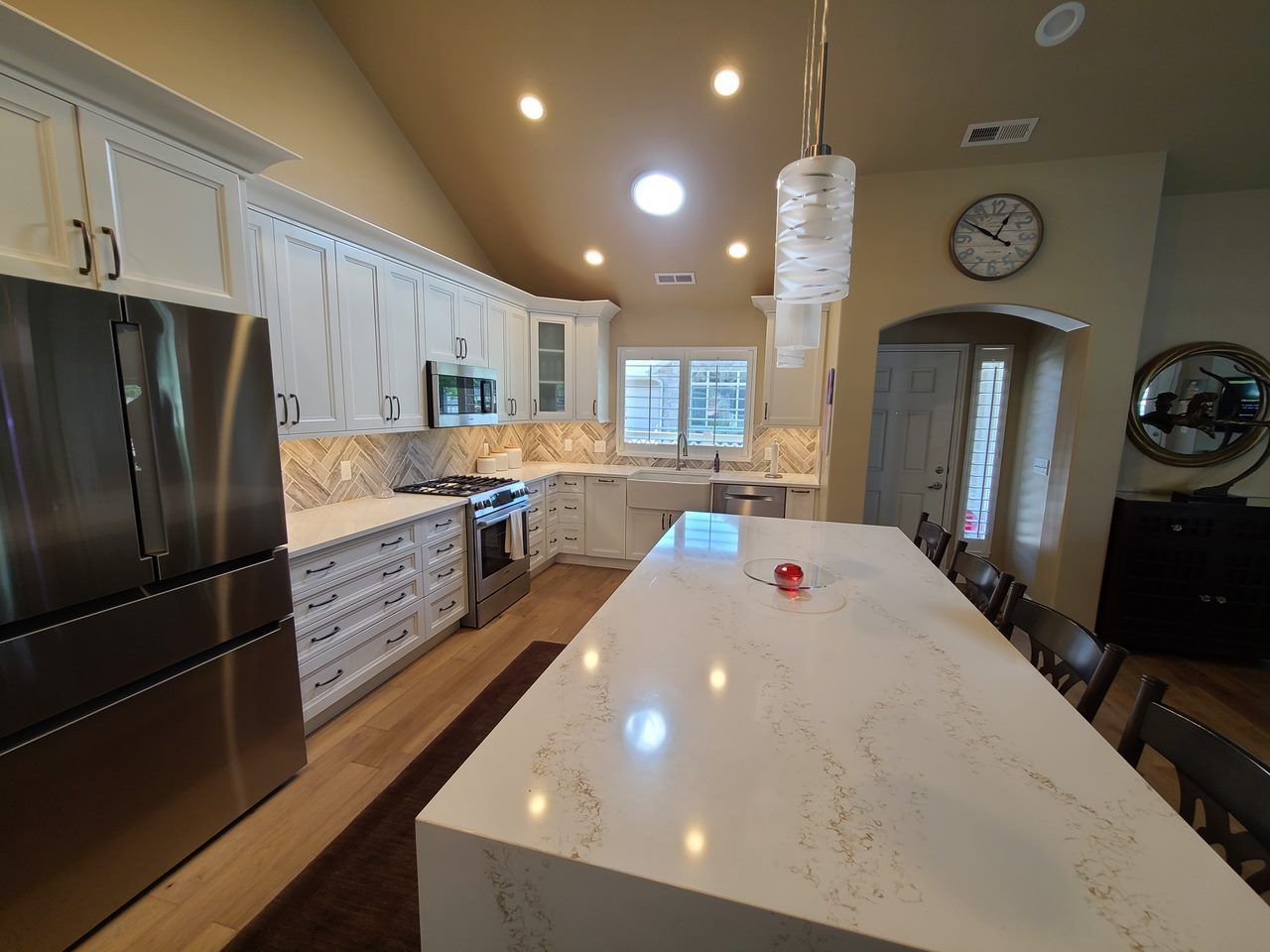 A kitchen with white cabinets , stainless steel appliances , a large island and a clock on the wall.