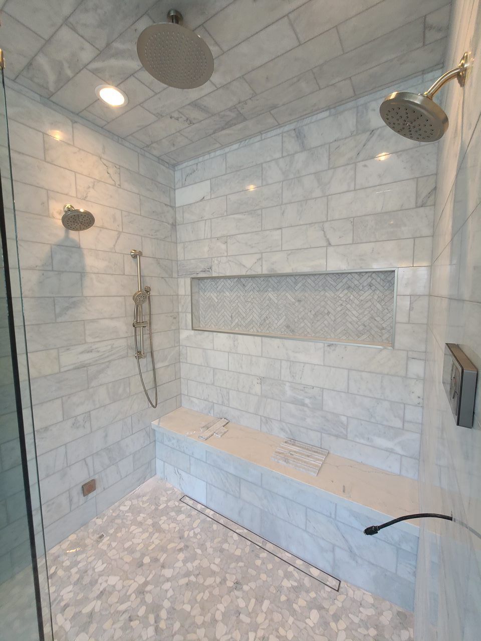 A shower with two shower heads and a bench in it.