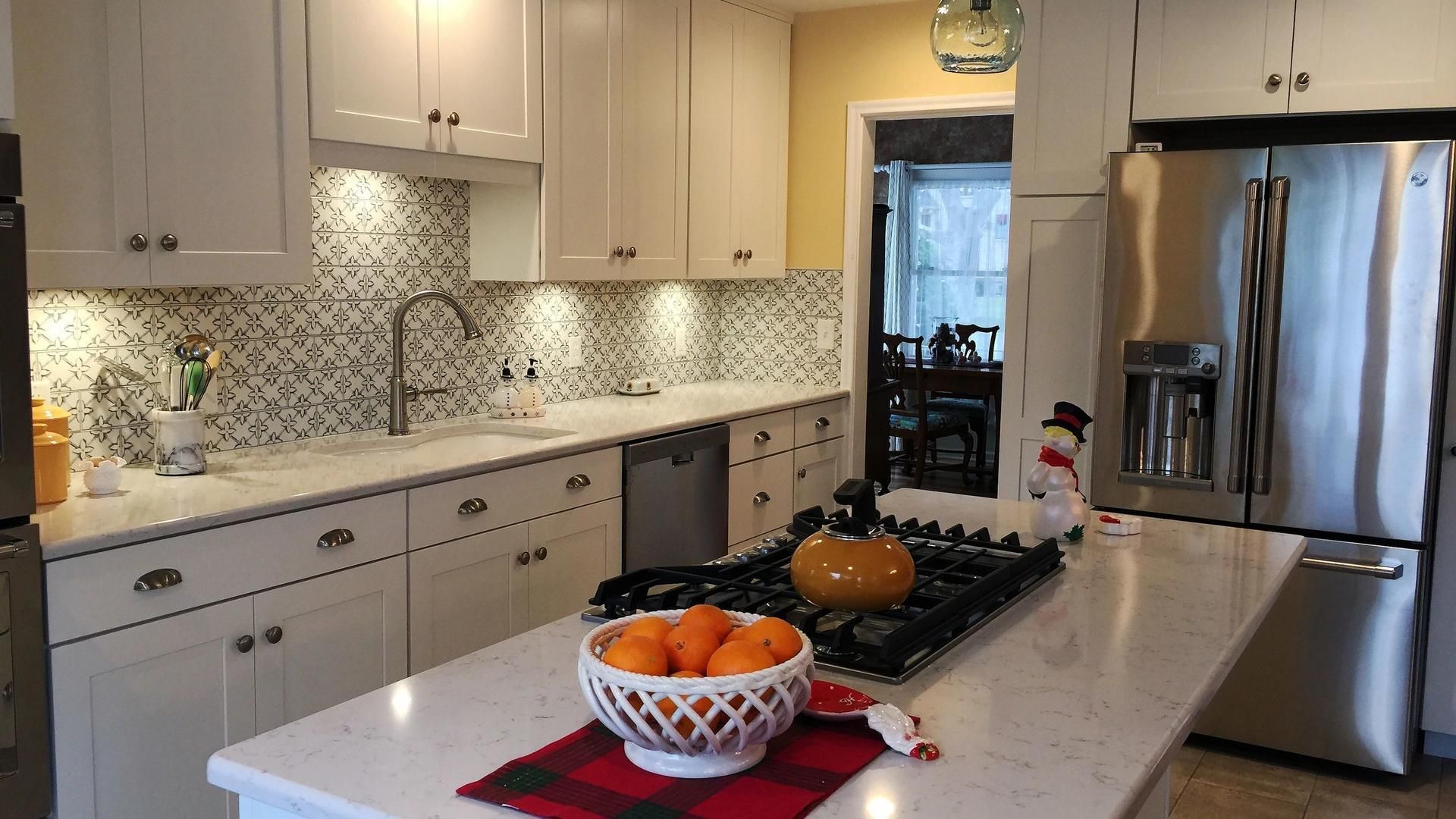 A kitchen with white cabinets and stainless steel appliances and a bowl of oranges on the counter.