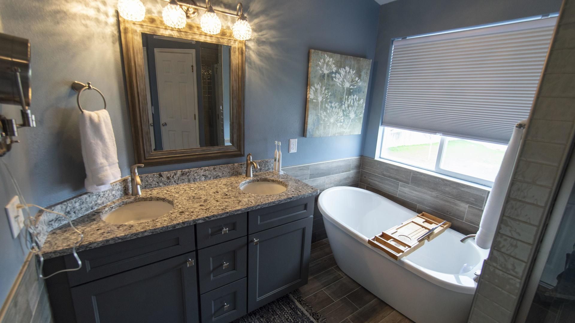 A bathroom with two sinks , a tub , a mirror and a window.