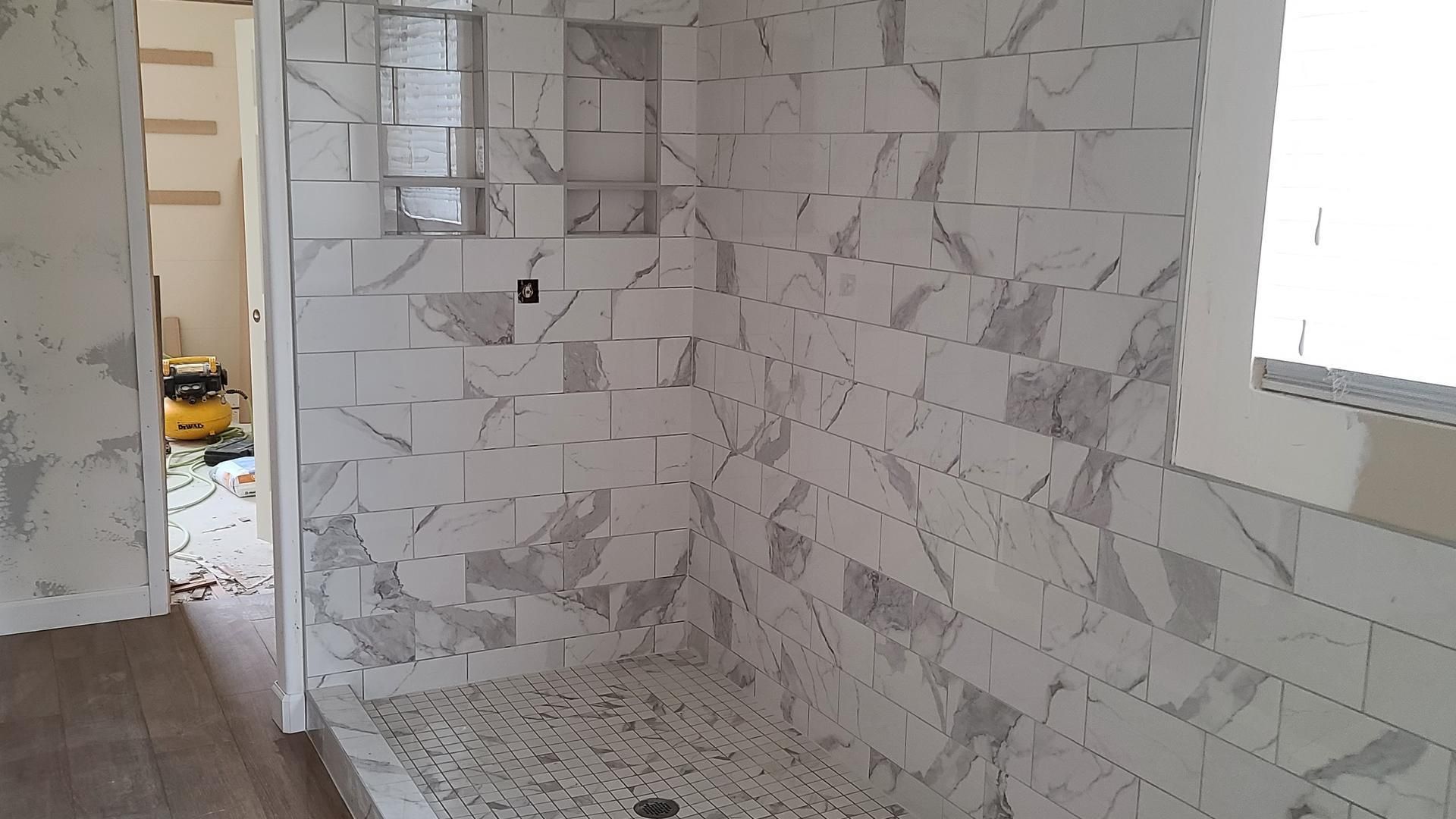 A bathroom with white tiles on the walls and a walk in shower.