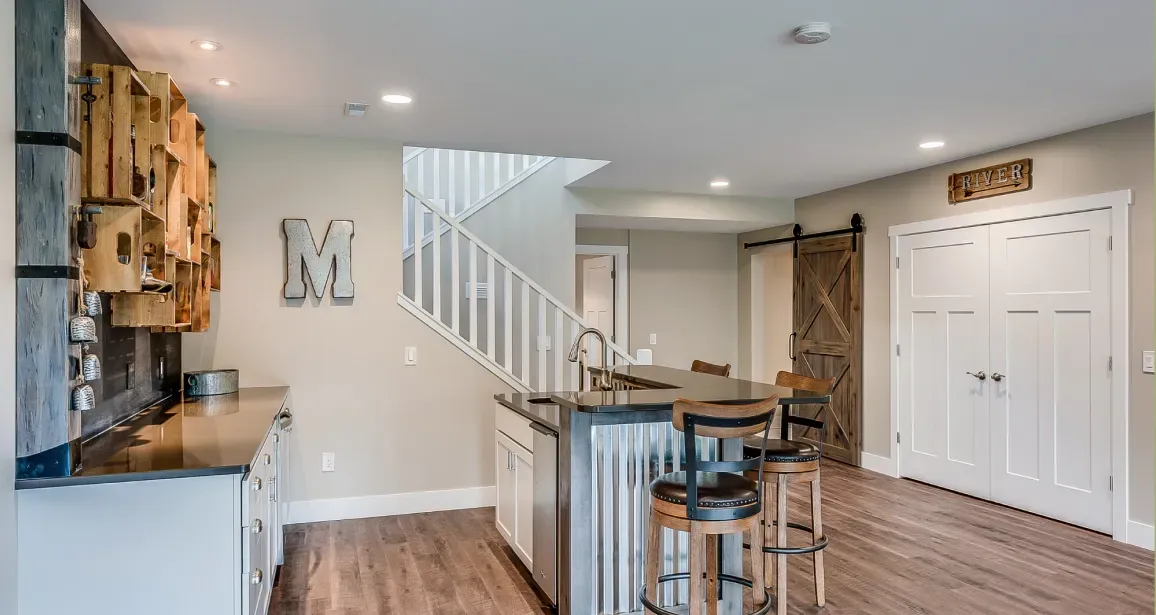A kitchen with a bar and stairs in a basement.