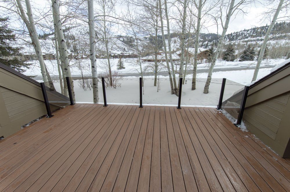 A wooden deck with a glass railing overlooking a snowy forest.