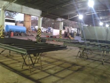 Estructuras de acero sobre caballetes en una fábrica. Al fondo, un tanque de agua y camiones.