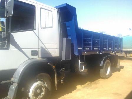 Camión volquete gris con caja azul en un día soleado.