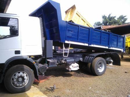 Camión volquete azul con cabina blanca, estacionado afuera.