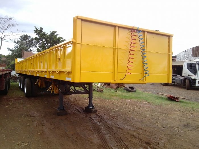 Remolque de plataforma amarillo sobre un terreno de tierra, con una escalera y líneas de aire enrolladas a un costado.