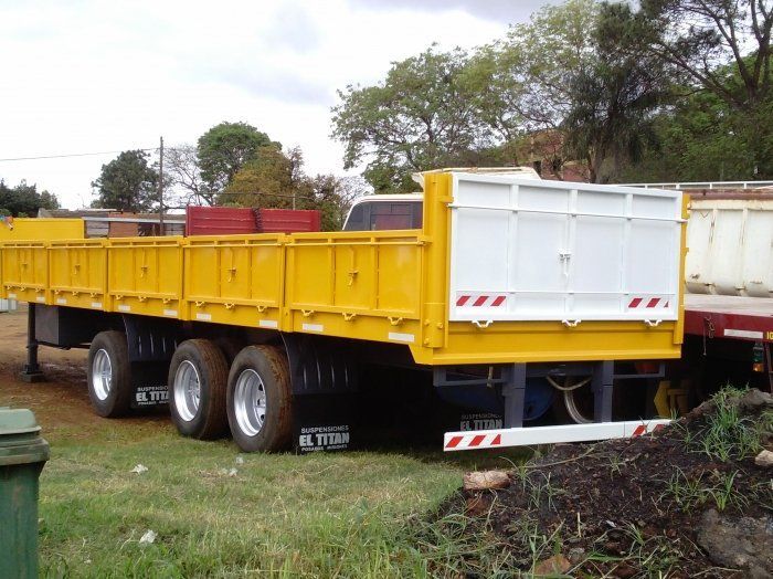 Remolque de plataforma amarillo y blanco estacionado sobre el césped.