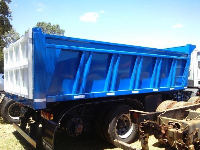 Camión volquete azul sobre un chasis negro con detalles en blanco, estacionada al aire libre en un día soleado.