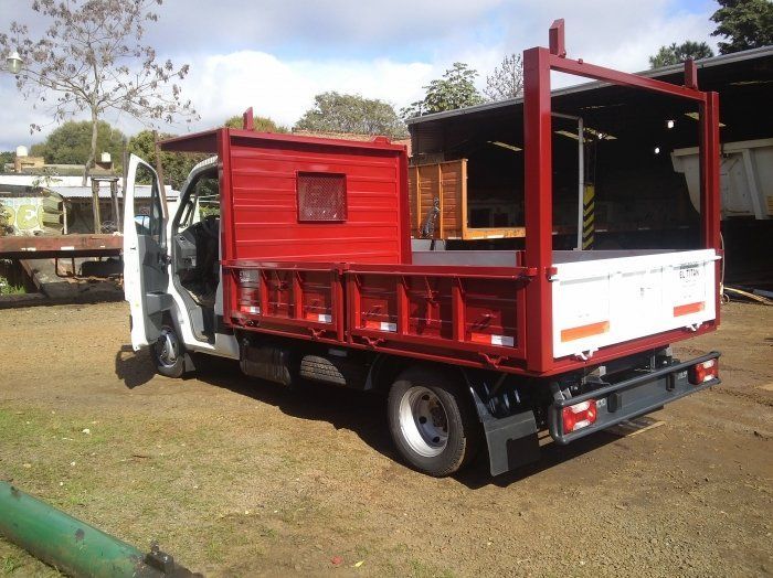 Camión utilitario rojo y blanco con las puertas abiertas, estacionado sobre el césped.