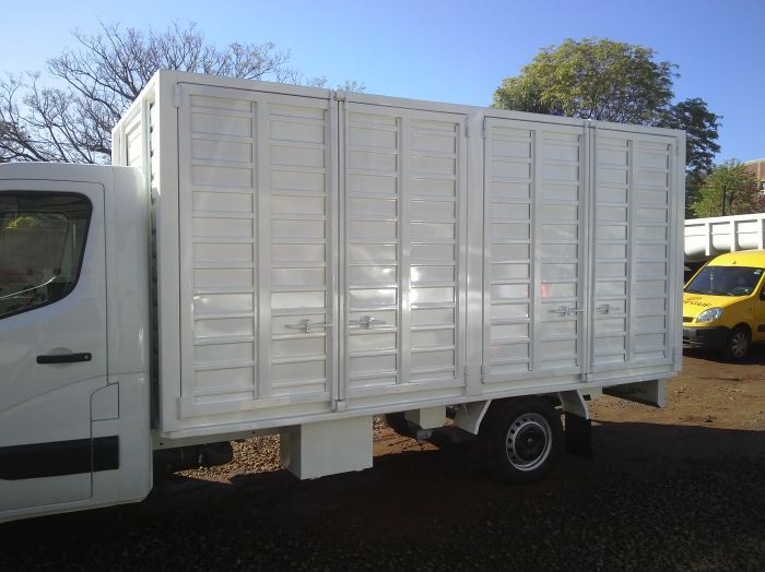 Camión de reparto blanco con puertas laterales con persianas estacionado al aire libre.