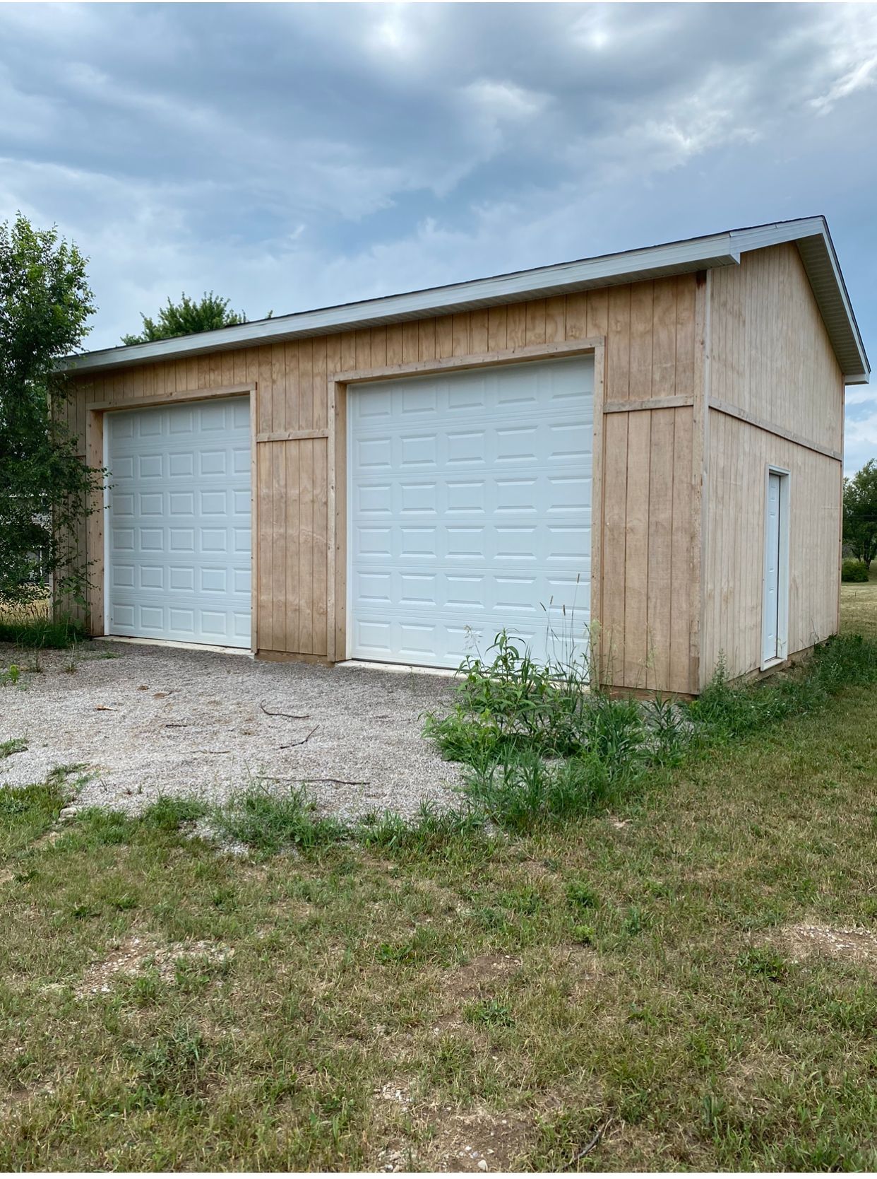 A garage with two white garage doors is sitting in the middle of a grassy field.