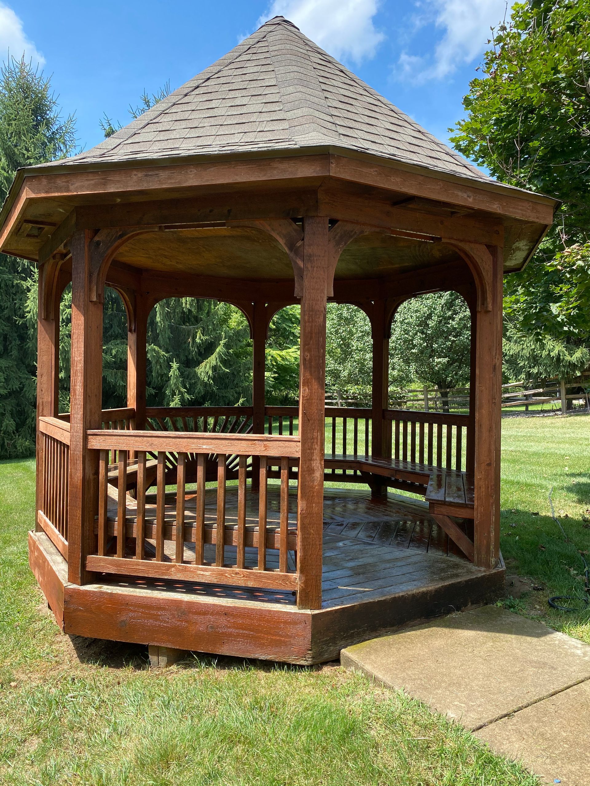 A wooden gazebo is sitting in the middle of a grassy field.