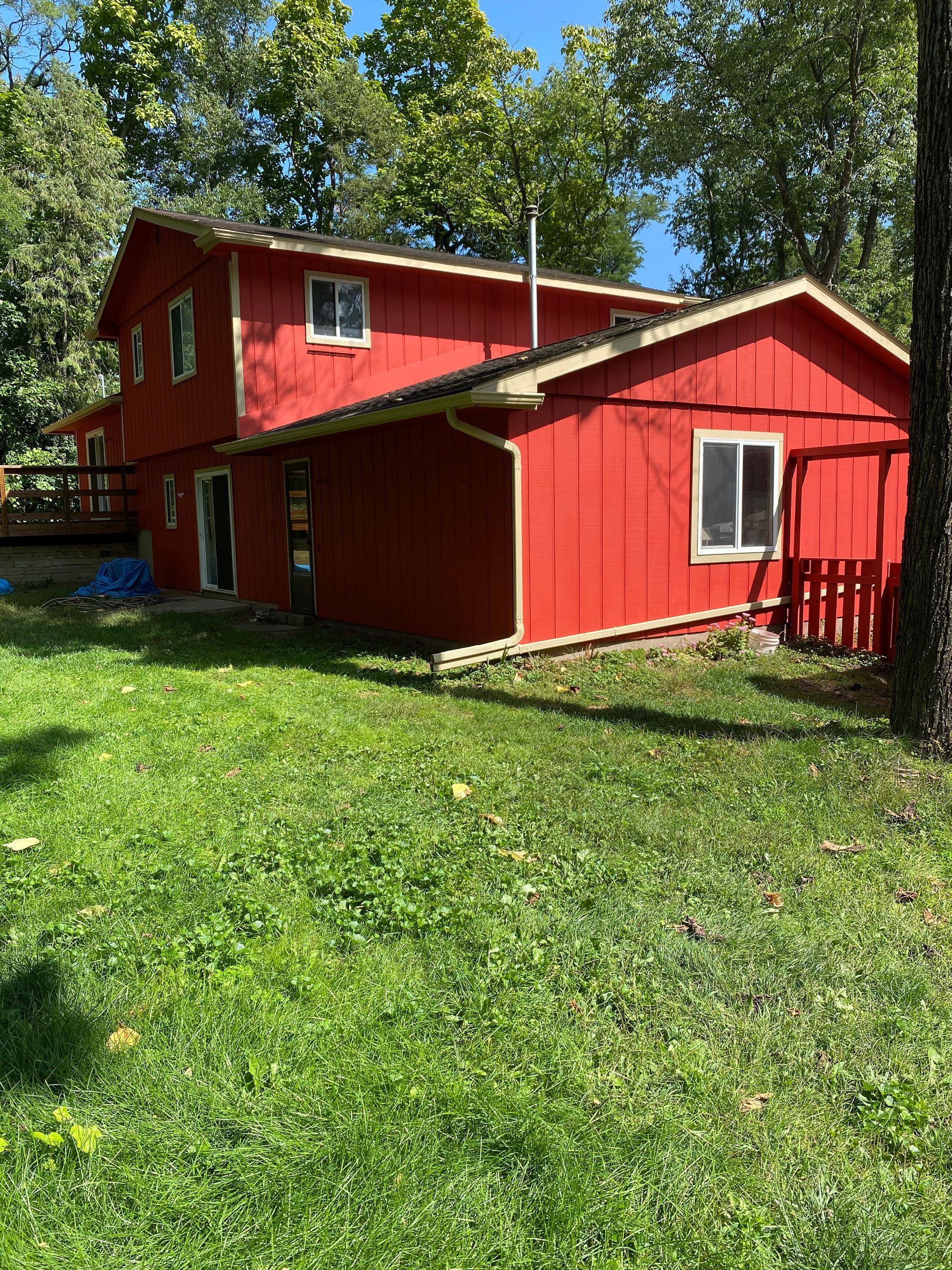 A red house is sitting in the middle of a lush green field.