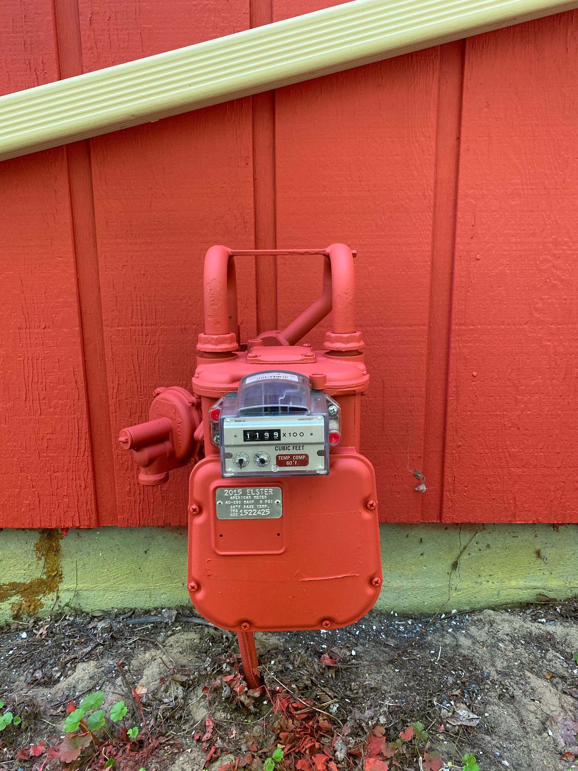 A red gas meter is attached to a red wall.
