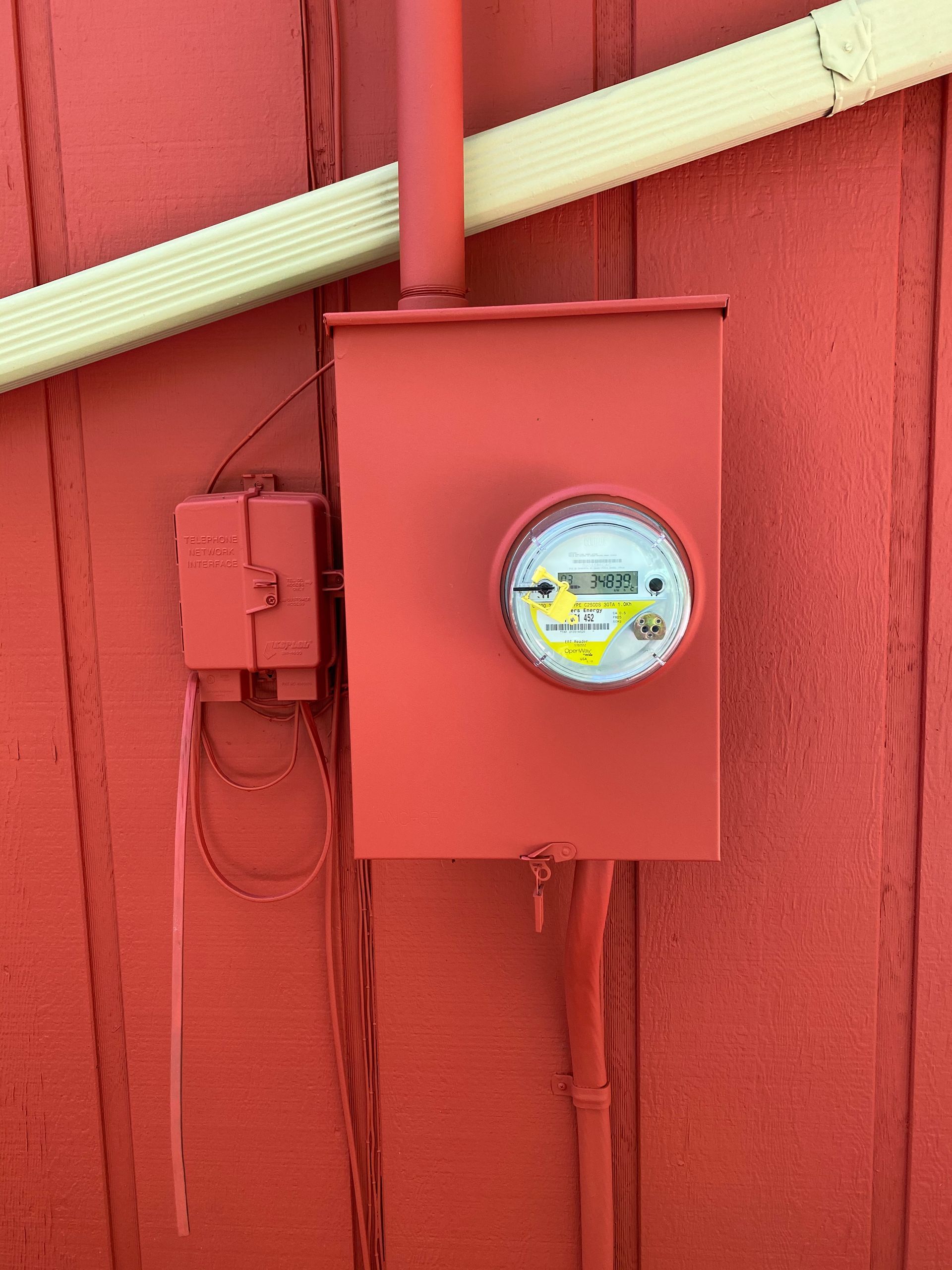 A red box with a meter on it is on a red wall.