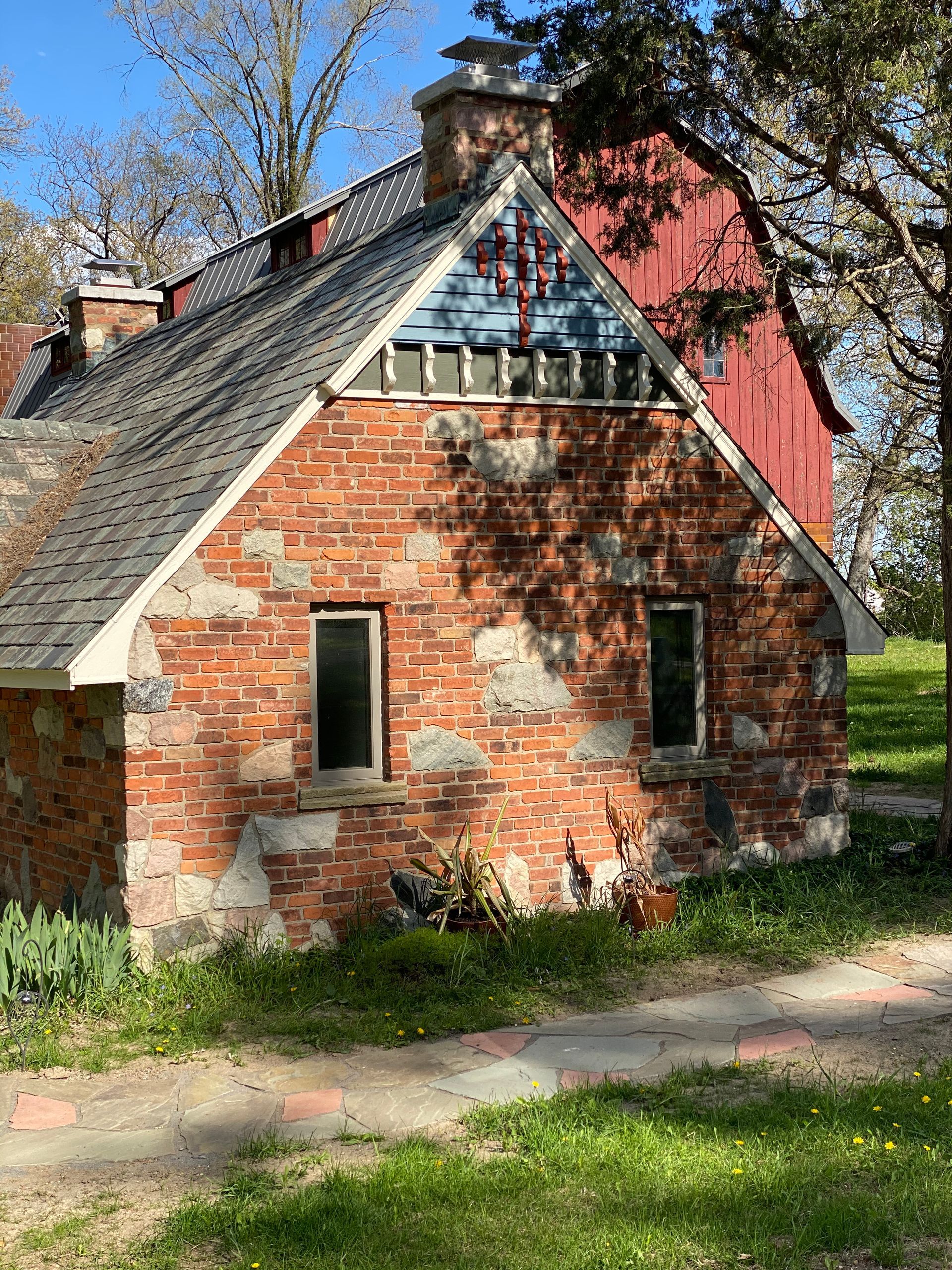 A small brick house with a red barn in the background.