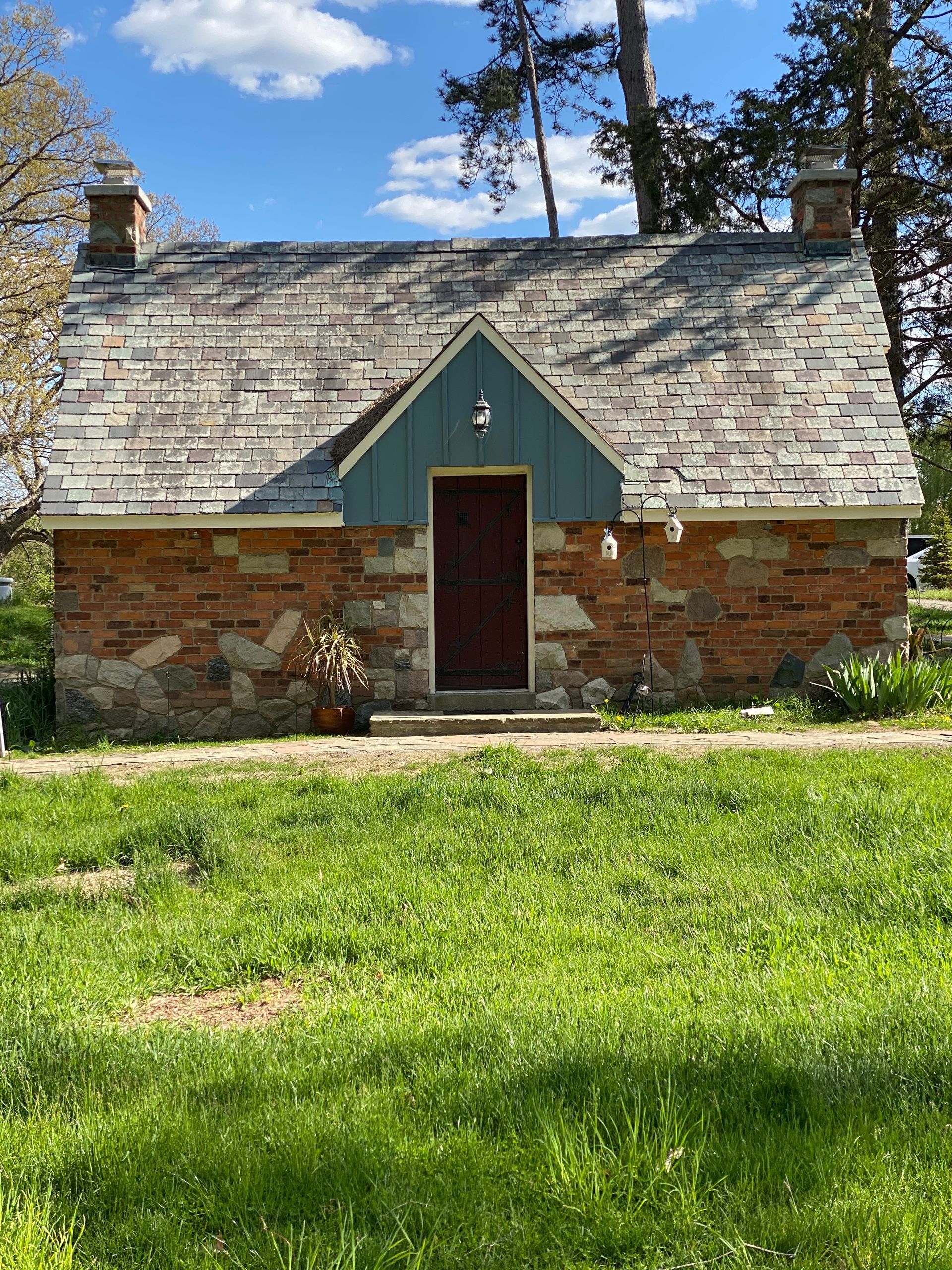 A small brick house with a green roof is sitting in the middle of a grassy field.