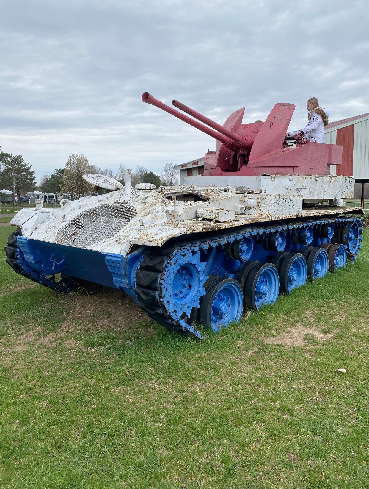 A red , white and blue tank is parked in a grassy field.