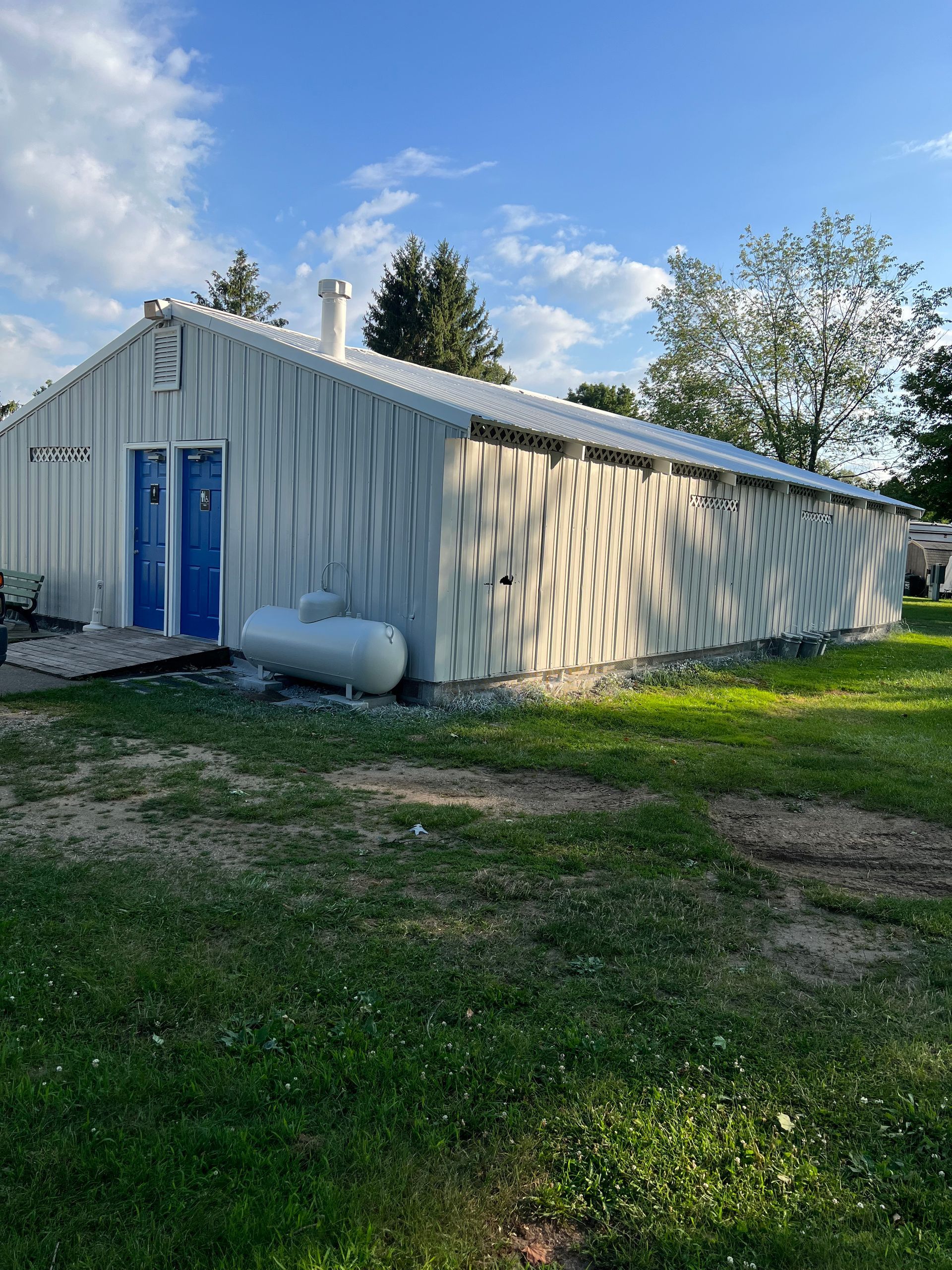 A white building with a blue door is sitting in the middle of a grassy field.